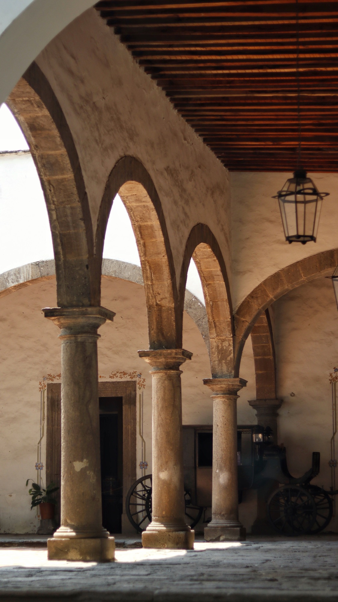 A sunlit historic courtyard lined with tall stone arches and columns